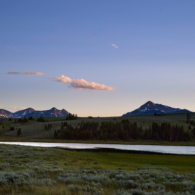 A beautiful mountain range behind a river against a lavender sky at dusk.