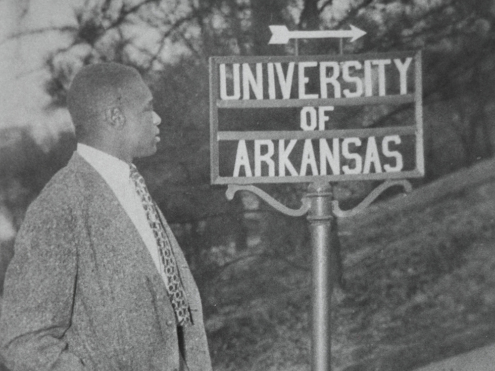 A black and white photo of Silas Herbert Hunt, a WWII veteran, in front of a sign for the University of Arkansas.
