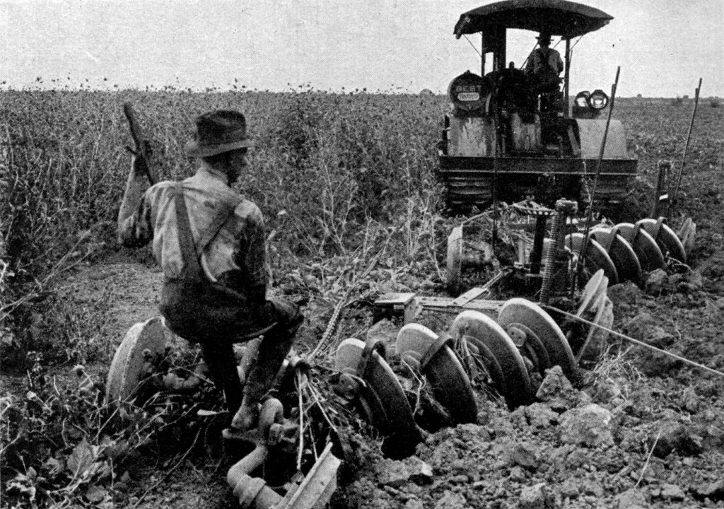 An old black and white photo of a man working in a field behind a plow.