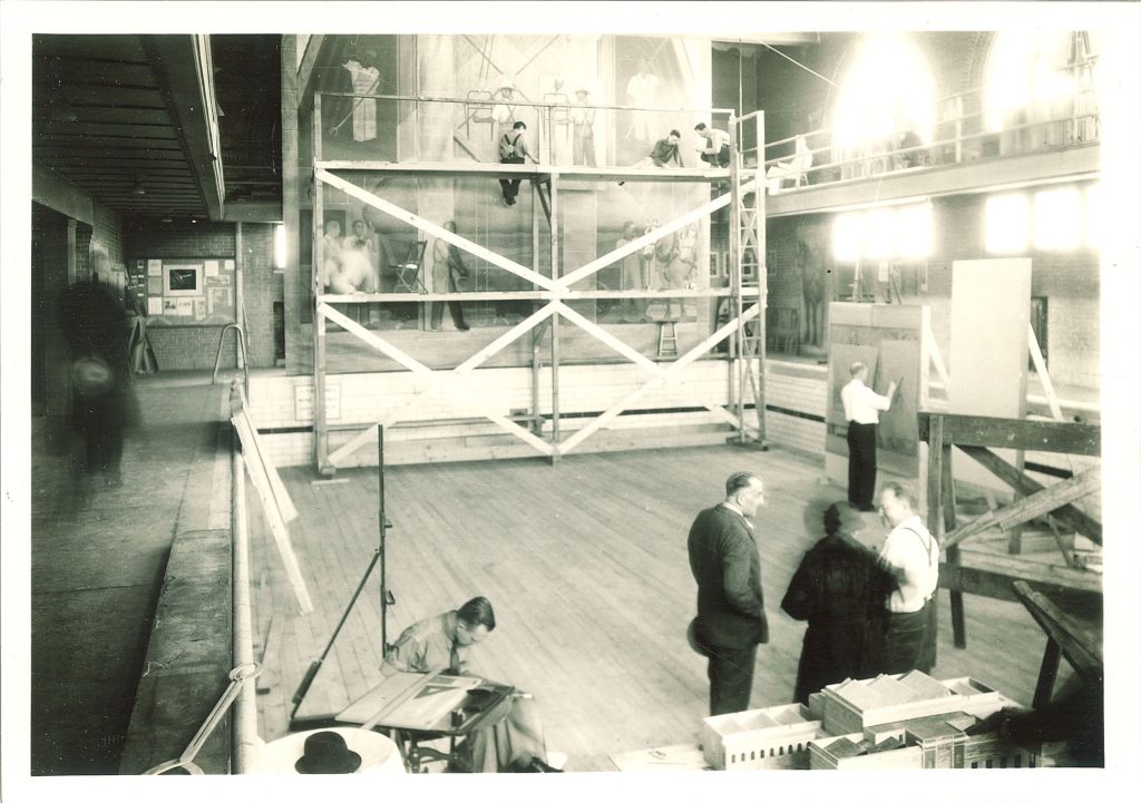 A black and white photo of a room under construction with people in suits milling around.