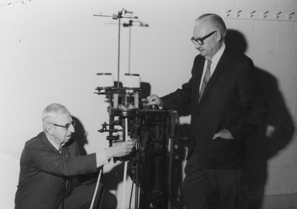 A black and white photo of two men with a machine.