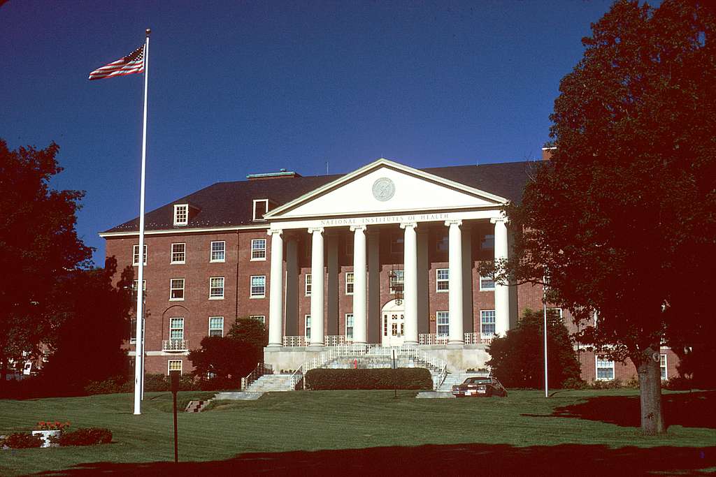 An older, aged photo of the building for the National Institutes of Health with an American flag flying out front.