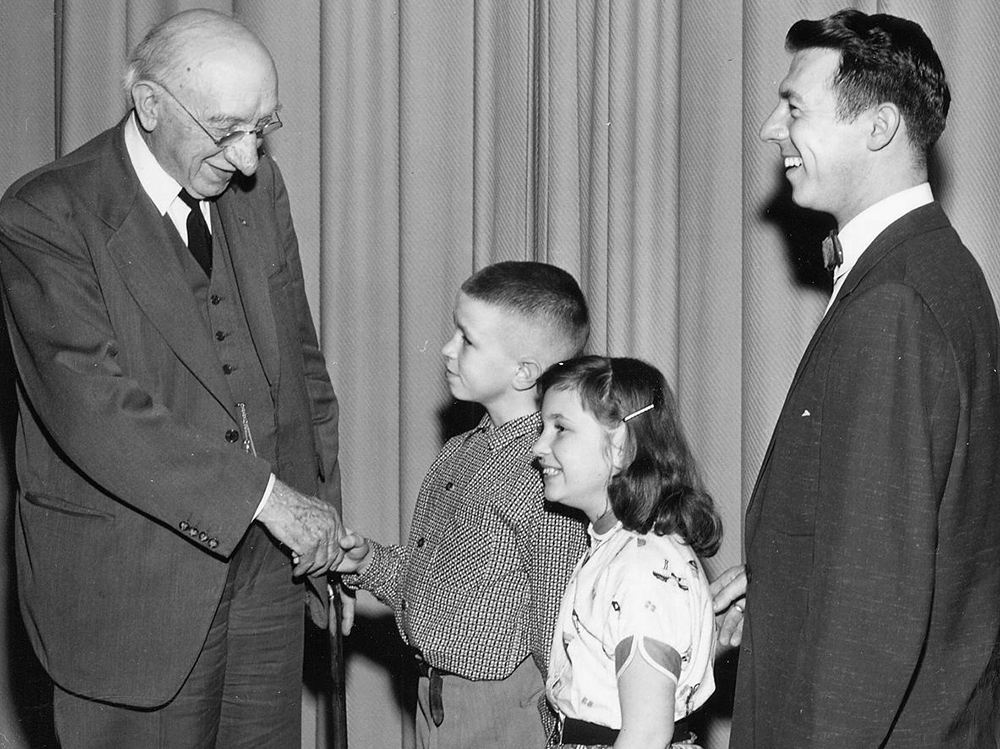A black and white photo of a man and two young children greeting an older man.