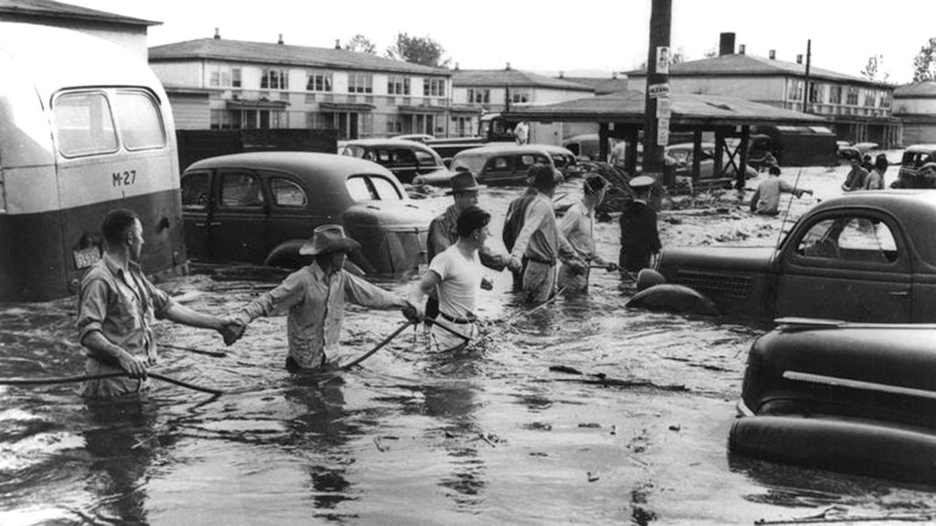 A black and white photo of people standing in flooded waters, banding together by their hands.