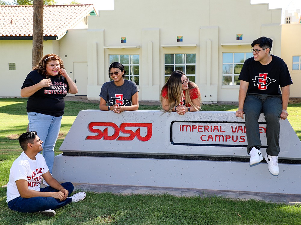 A few students sitting on and around a sign for SDSU's Imperial Valley campus.