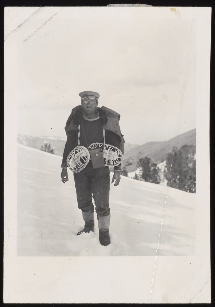 A black and white photo of a man on a snowy mountain with show shoes.