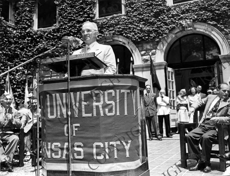 A photo of someone giving a speech behind a podium labeled "University of Kansas City".