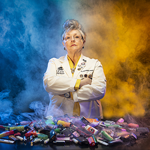 A female forensic toxicologist standing in front of a pile of vapes in a white lab coat.