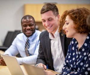 Three adult learners collaborate in front of a laptop
