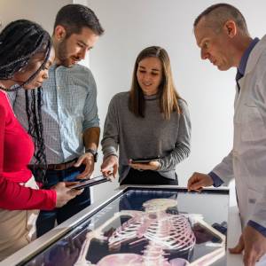 A team of students and a scientist standing over an image of a skeleton.
